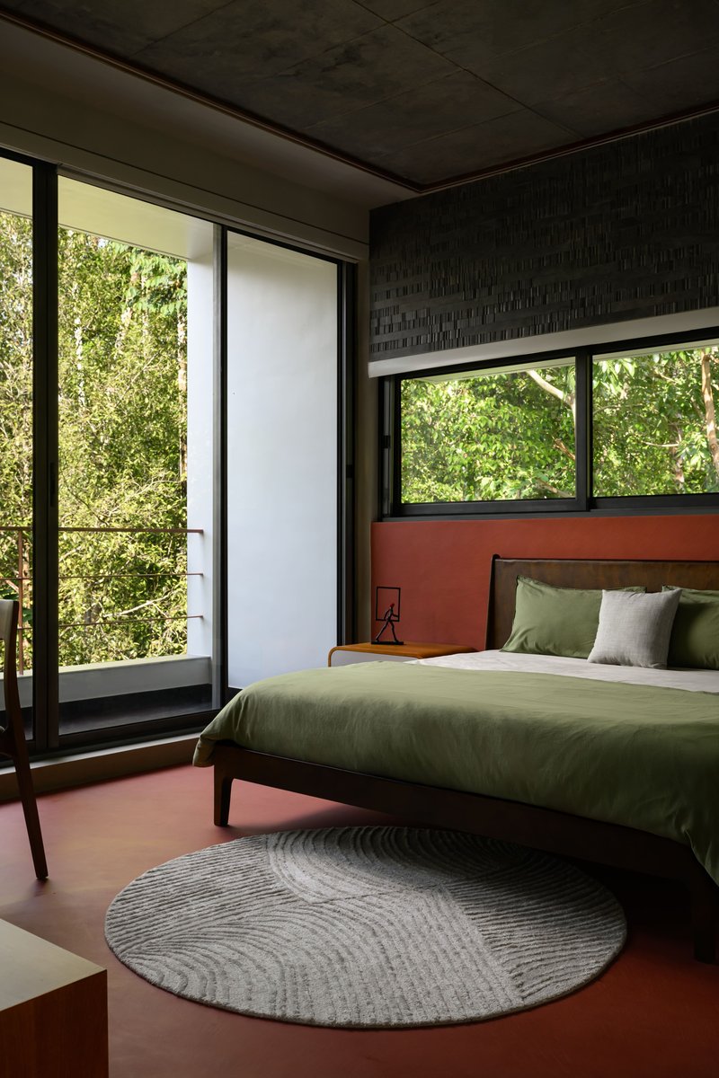 Corner bedroom with terracotta flooring and full-height glazing to a private balcony surrounded by greenery