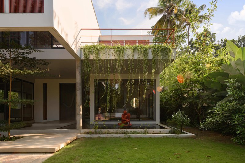 Garden courtyard with seated figure beside a water feature under trailing vines and palm trees