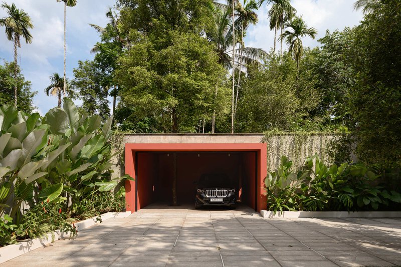 Recessed garage with coral-painted frame set into a concrete retaining wall surrounded by palms and tropical planting