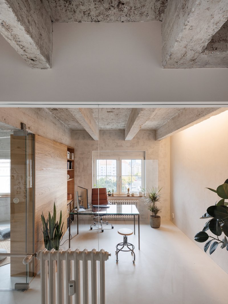 Long interior corridor with exposed concrete beams, white radiators, and desk area by the window