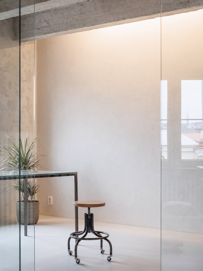 Interior workspace with glass partition, adjustable stool, potted plant, and exposed concrete ceiling beams