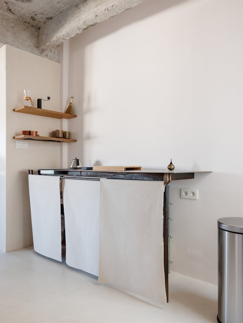 Compact kitchenette with white cabinet doors, timber shelving, and exposed concrete ceiling above
