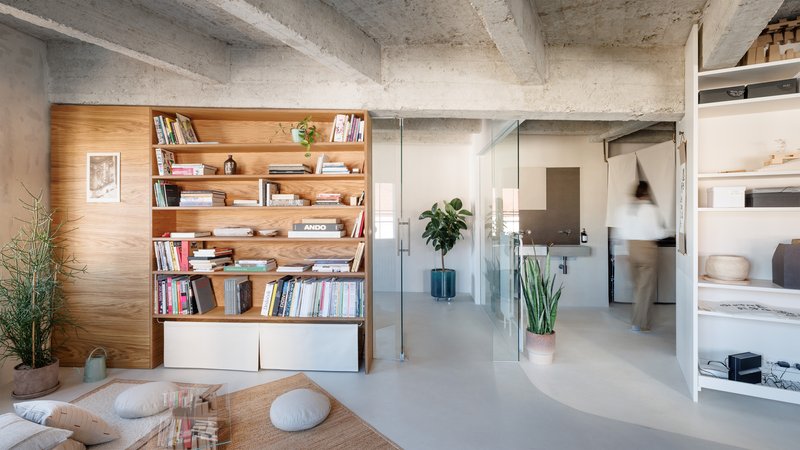 Timber bookshelf wall beside a glass partition with a figure walking through the background