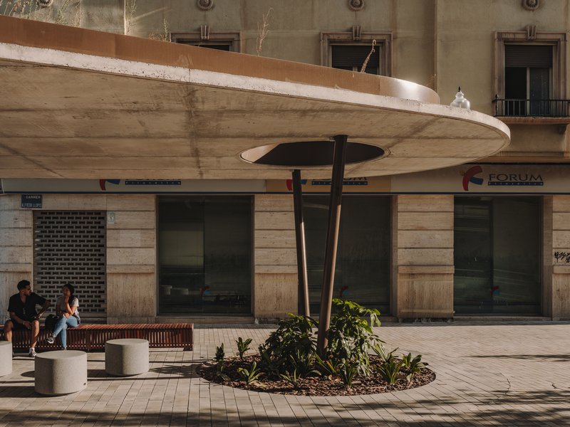 Concrete canopy with circular opening and central support column beside timber bench seating at dusk