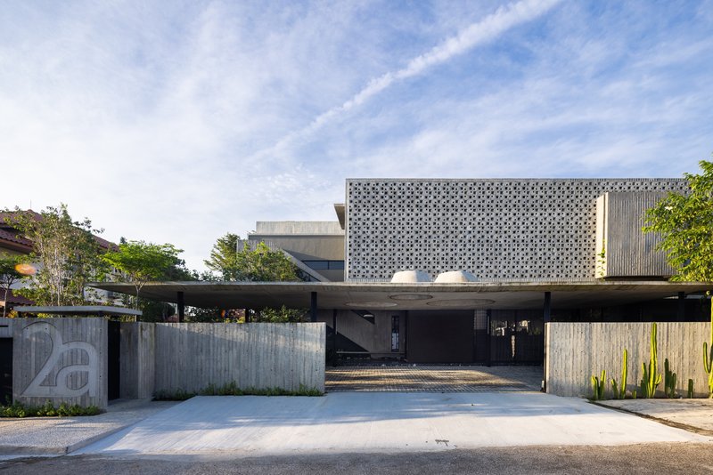 Street view of the perforated concrete screen facade above a cantilevered carport and board-formed concrete wall