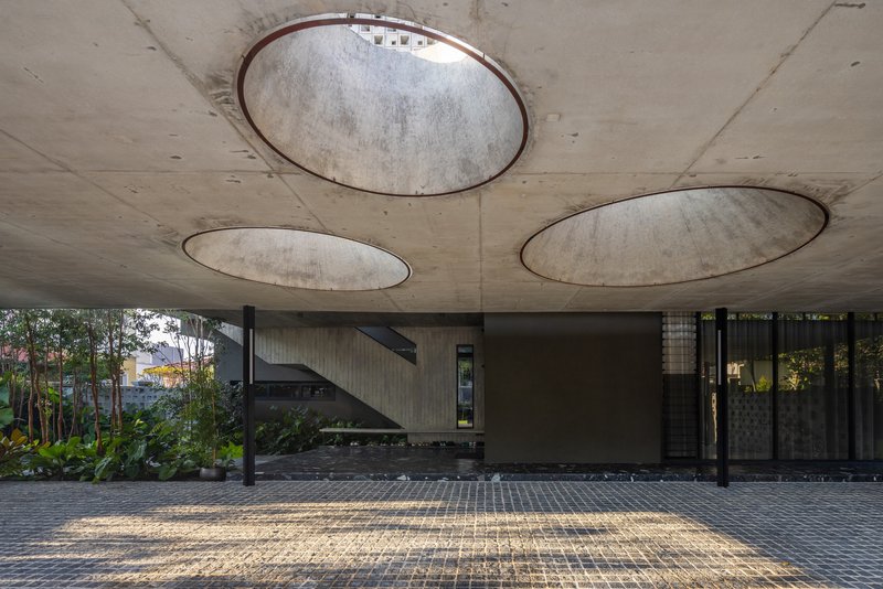 Covered carport with circular skylights cut into the board-formed concrete soffit above a paved driveway