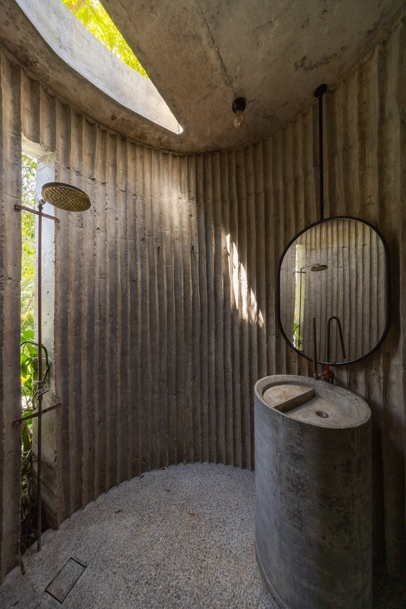 Curved bathroom enclosure with fluted concrete walls, circular sink, round mirror, and skylight casting morning light
