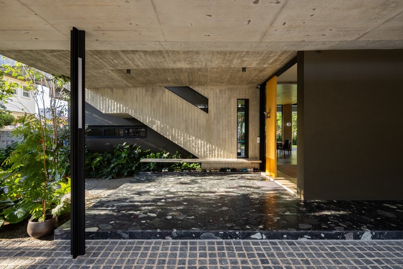Black steel staircase against a board-formed concrete wall with dappled sunlight from overhead openings