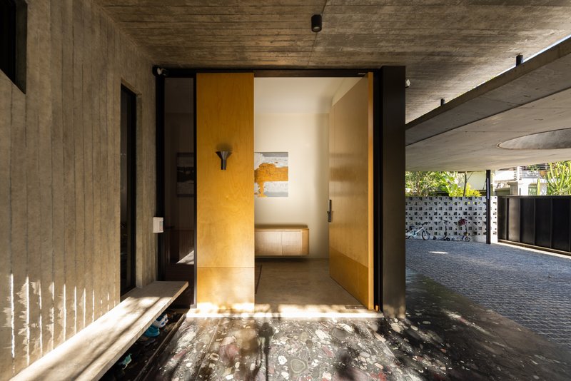 Entry threshold with warm plywood interior walls viewed from the dark stone floor under concrete soffit