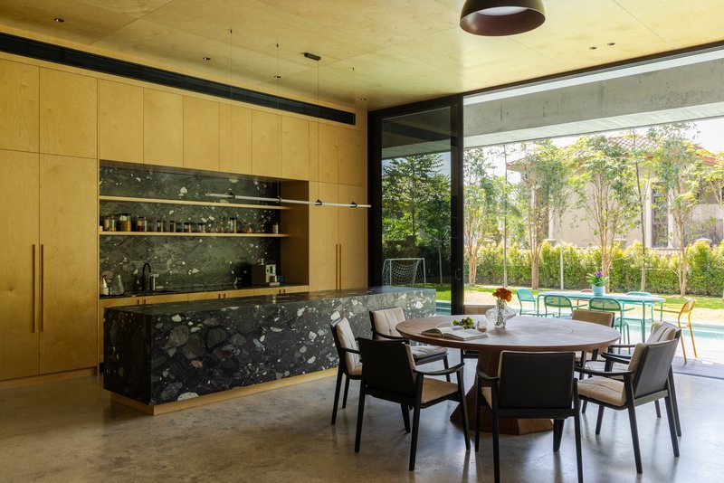 Kitchen and dining area with terrazzo island and plywood cabinetry opening to a garden courtyard