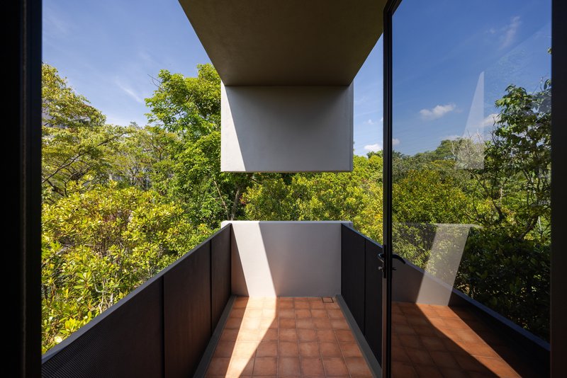 Balcony terrace with terracotta tiles framed by dark metal railings and a view into foliage