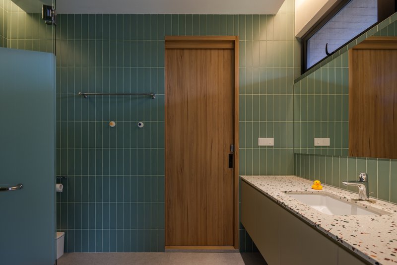 Bathroom with green tile walls, timber door, and terrazzo vanity beneath a mirrored cabinet