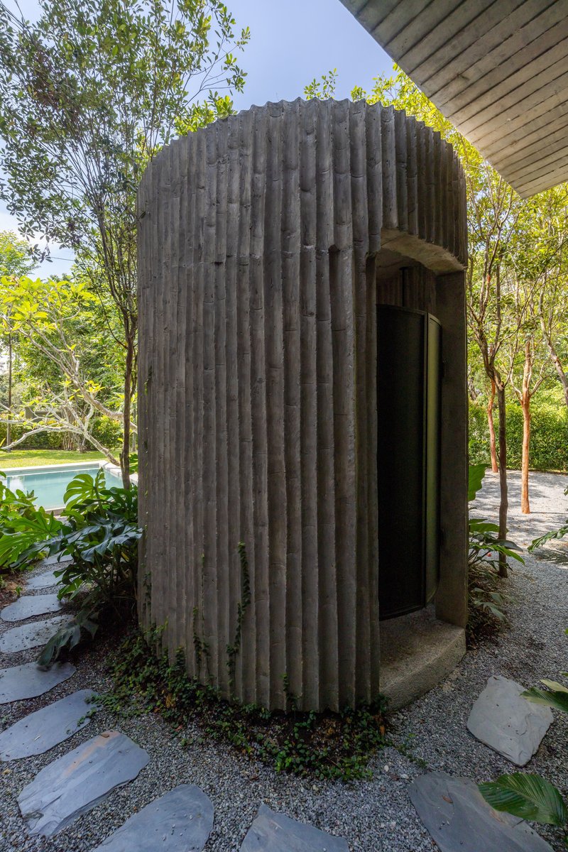 Cylindrical concrete tower with vertical ribbing surrounded by trees and gravel pathways