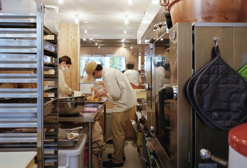 Staff working at stainless steel prep counter in narrow kitchen with track lighting overhead