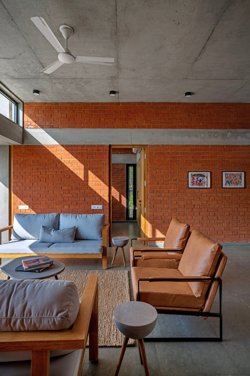 Double-height living room with red brick walls, exposed concrete ceiling, and sunlight through clerestory windows