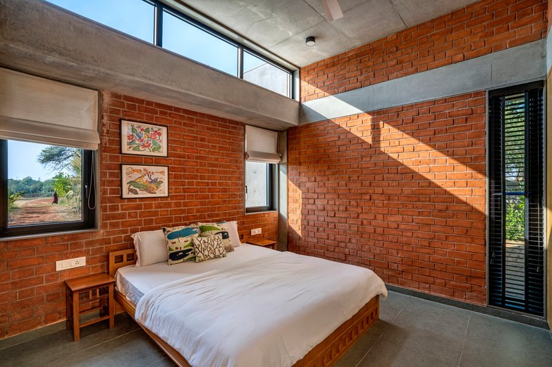 Bedroom with red brick walls, concrete ceiling beam, and clerestory windows casting geometric shadows