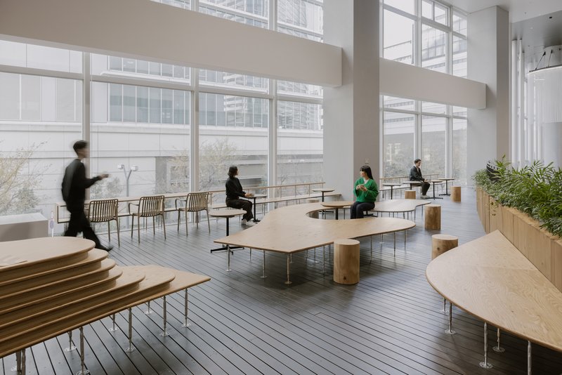 Open seating area with kidney-shaped plywood tables and wire-backed chairs facing clerestory windows in muted daylight