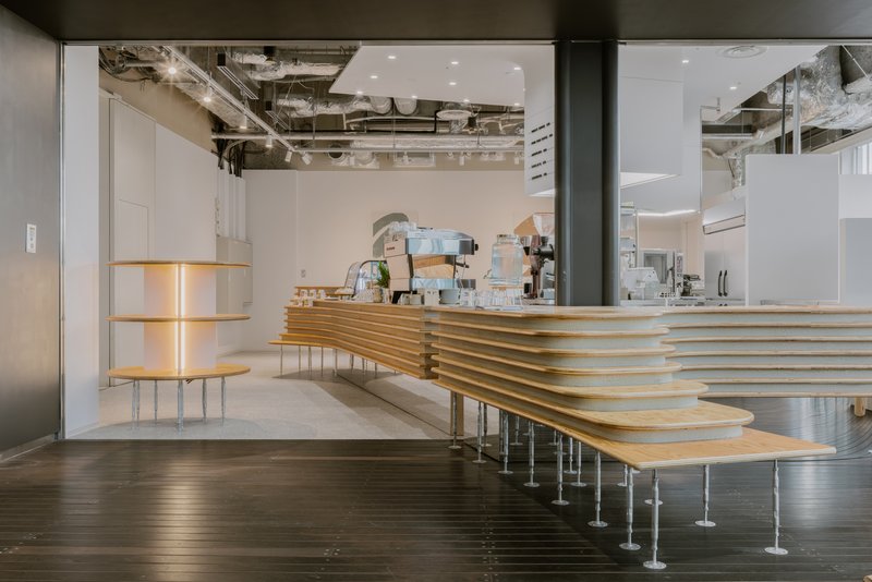 Laminated plywood service counter with horizontal ribbing on steel legs beneath exposed concrete ceiling