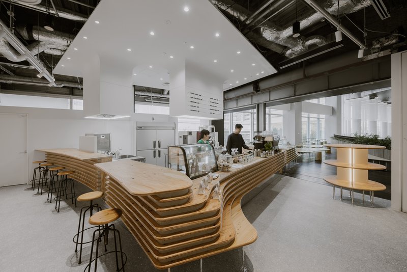 Cafe interior with layered timber counter and stools beneath exposed industrial ceiling systems