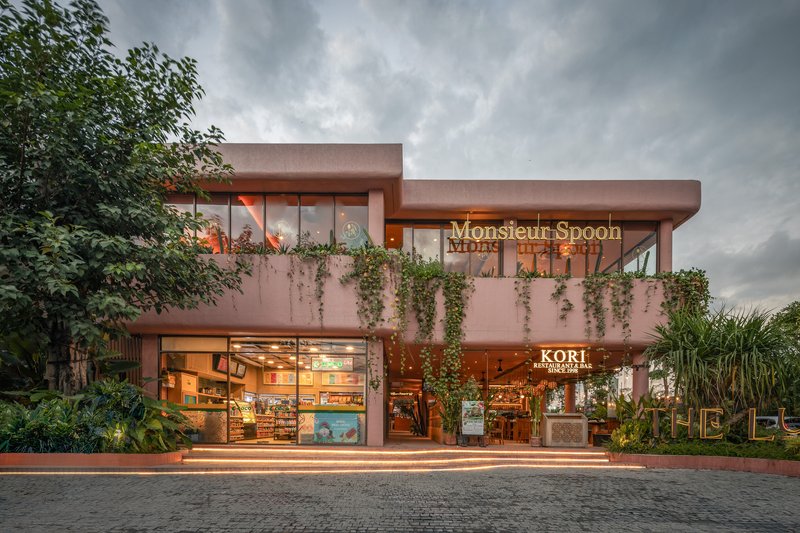Two-story retail facade with flat overhanging roof and illuminated storefronts at dusk under heavy clouds