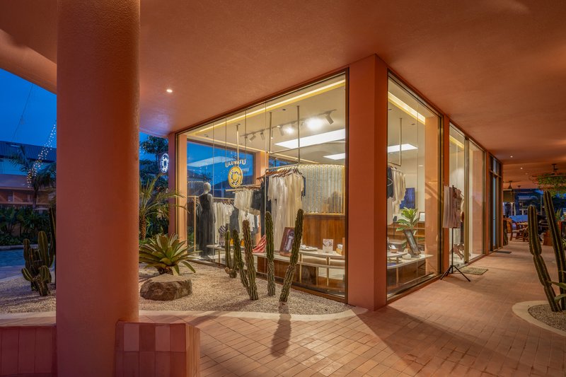 Covered walkway with terracotta columns and ceiling overlooking glazed storefront and planted gravel beds at dusk