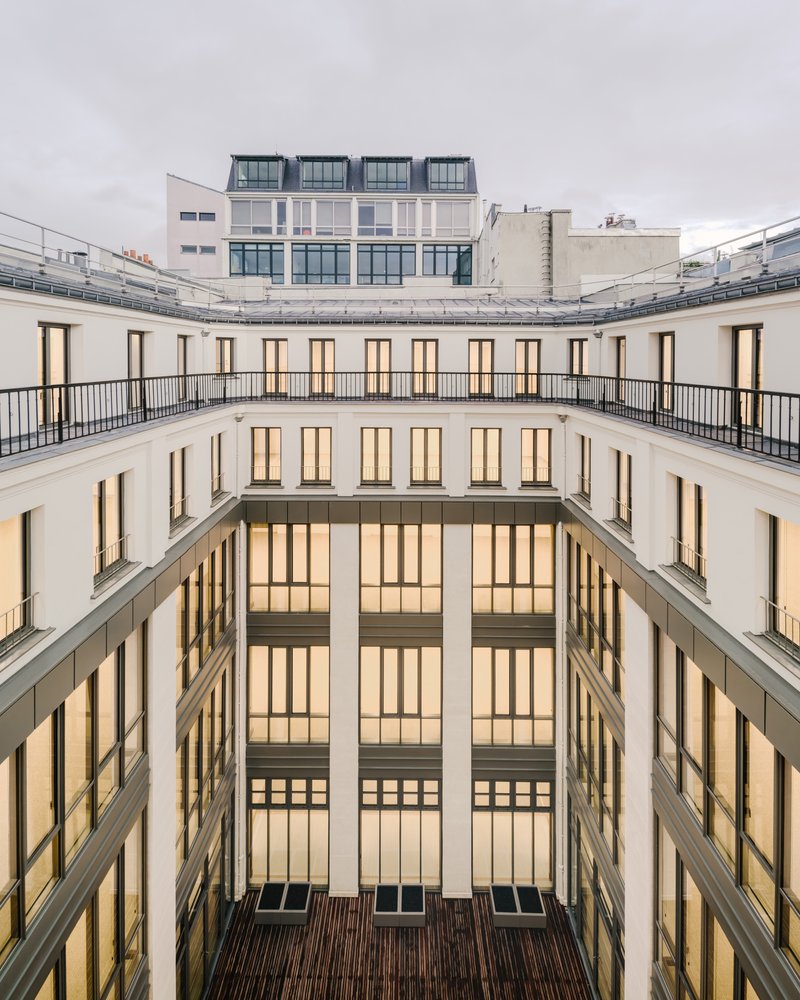 Interior courtyard with cream facades, tall windows, metal balconies and timber decking at the base under overcast sky