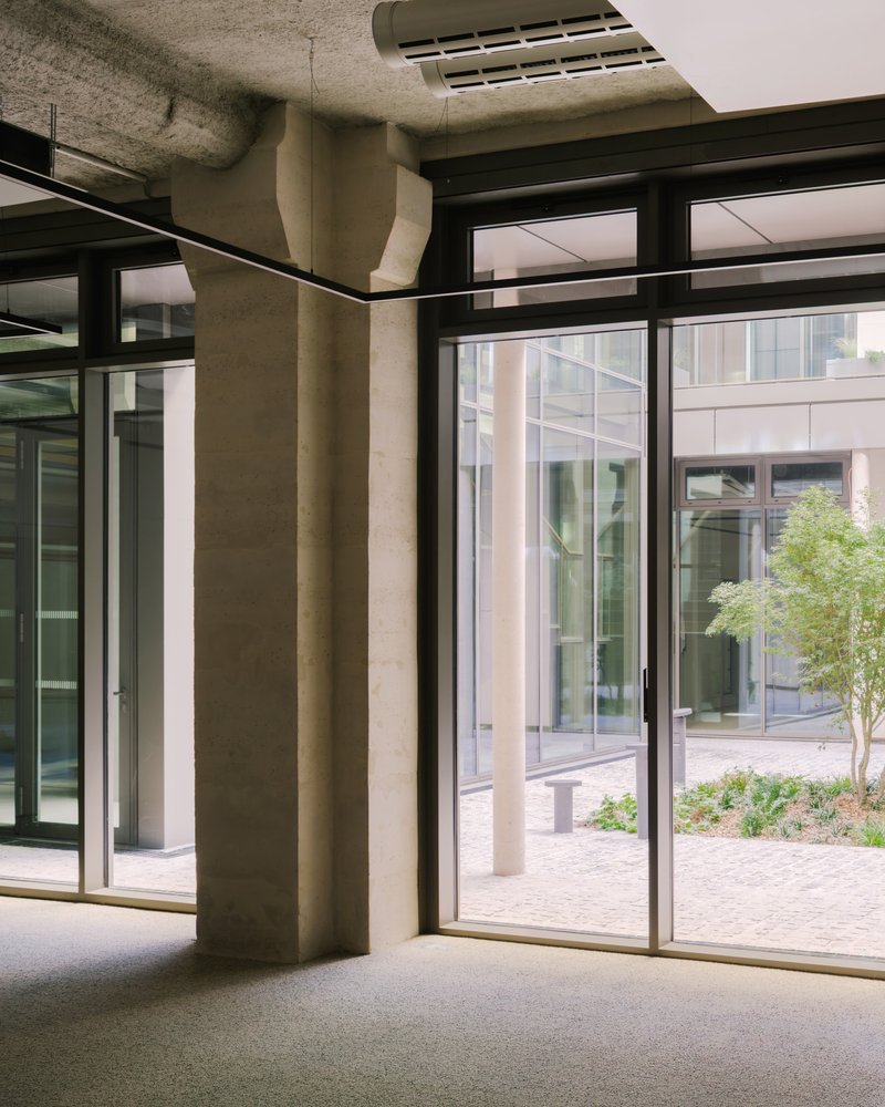 Ground floor interior with exposed concrete columns, black framed glazing overlooking planted courtyard outside