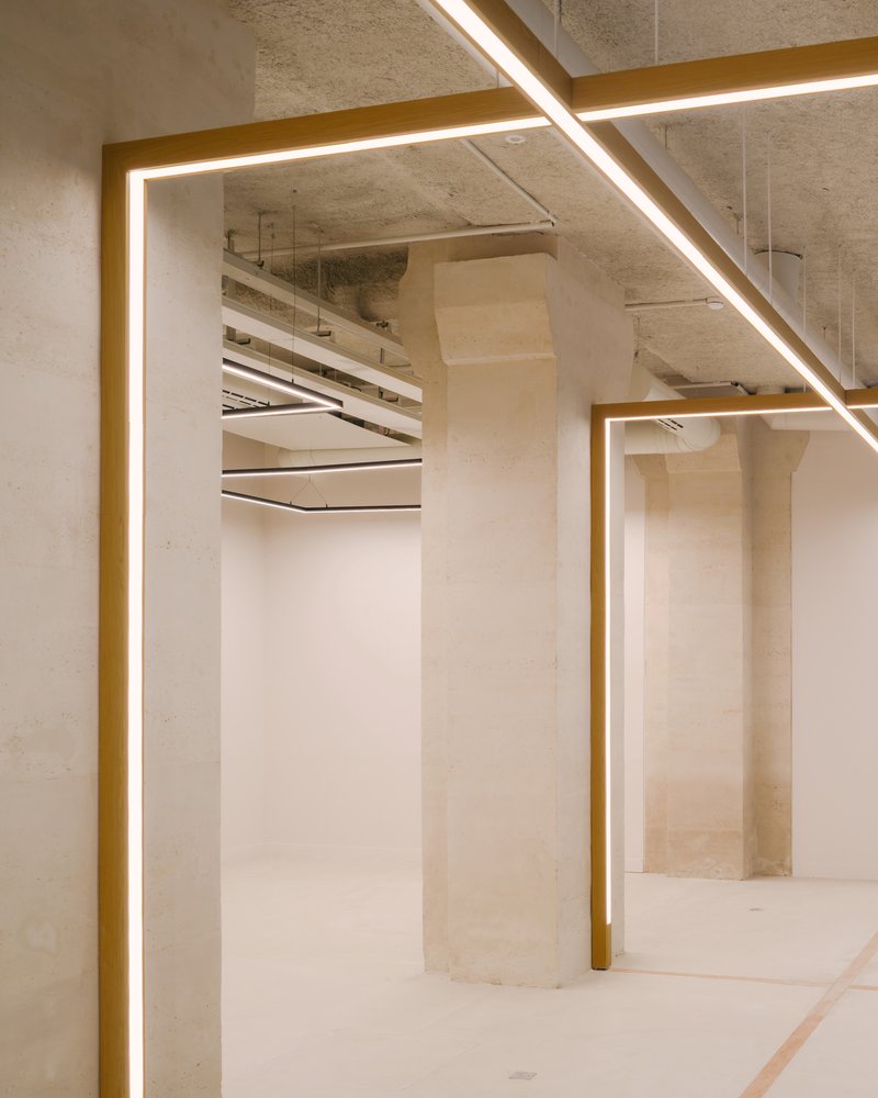 Concrete interior with brass-edged illuminated frames around columns and exposed ceiling services above