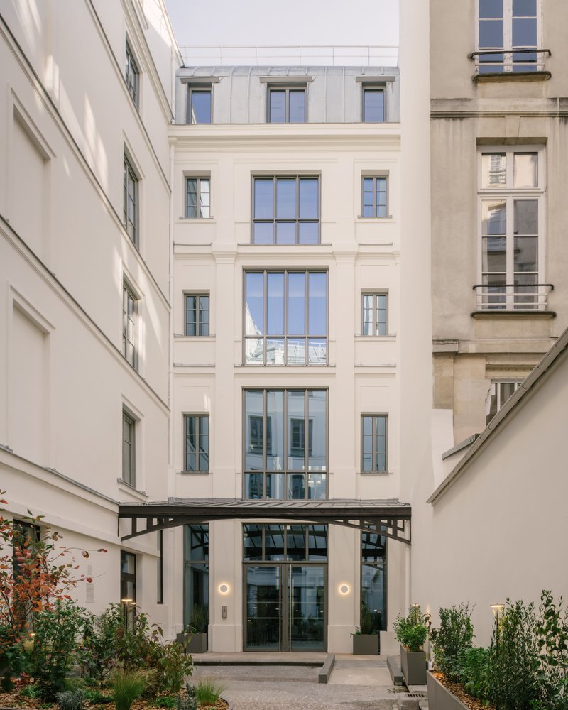Courtyard entry facade with glazed opening beneath a steel canopy and planted beds on either side