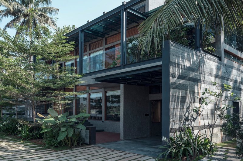 Two-story concrete and timber facade with steel frame pergola surrounded by palm fronds and tropical planting