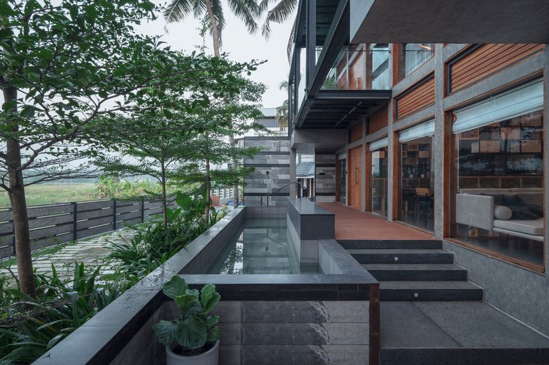 Stepped terrace with dark stone slabs and shallow water channel alongside timber and glass facade