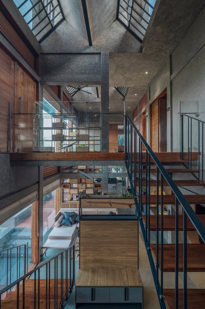Double-height interior void with timber and steel stairs connecting stacked platforms under concrete ceiling