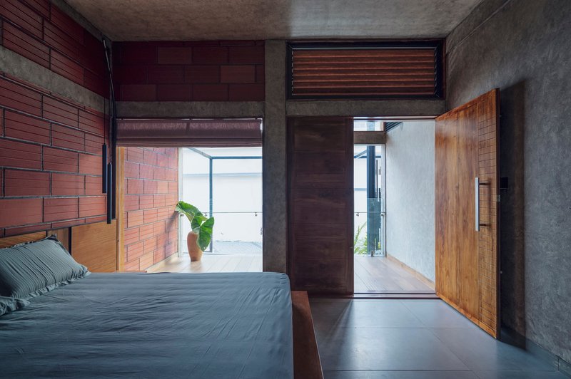 Bedroom with exposed brick wall and polished concrete floor opening to corridor beyond timber door