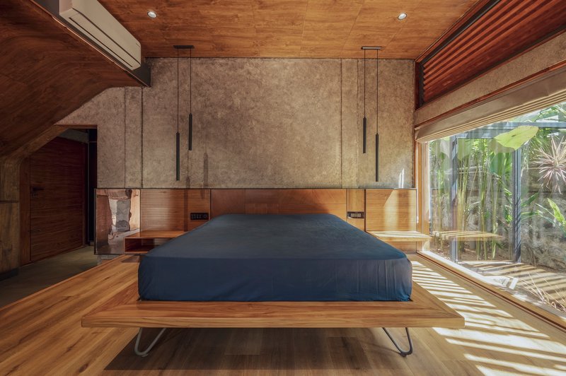 Bedroom with platform bed and timber ceiling receiving dappled sunlight through glazed wall to planted courtyard