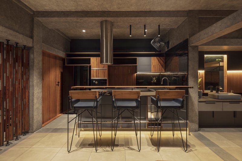 Open kitchen with central island and wire-frame stools under recessed concrete ceiling at night