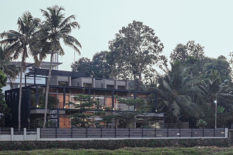 Street elevation showing layered concrete floors and glass walls framed by palm trees and tropical foliage
