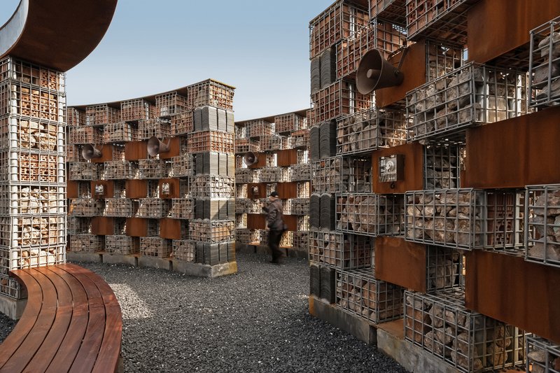 Interior courtyard enclosed by gabion walls filled with stone and punctuated by corten steel panels