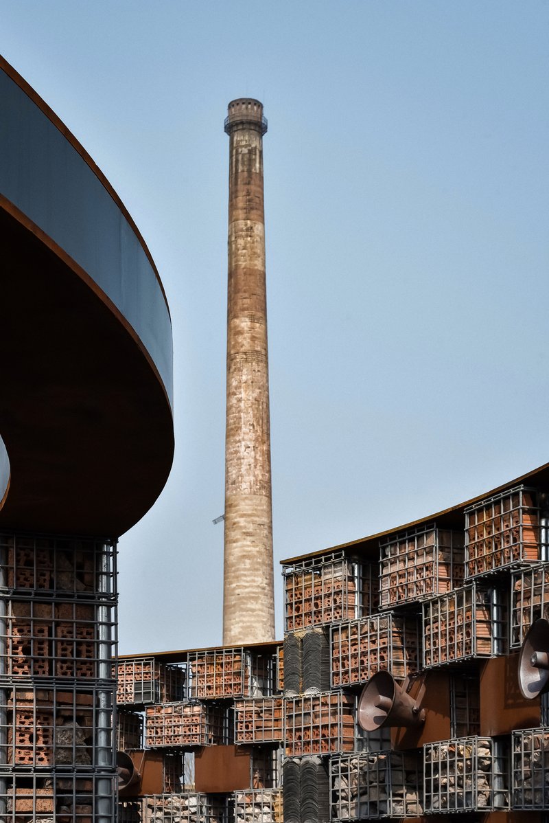 Weathered brick chimney rising behind a curving canopy and gridded brick screen wall with corten steel frames