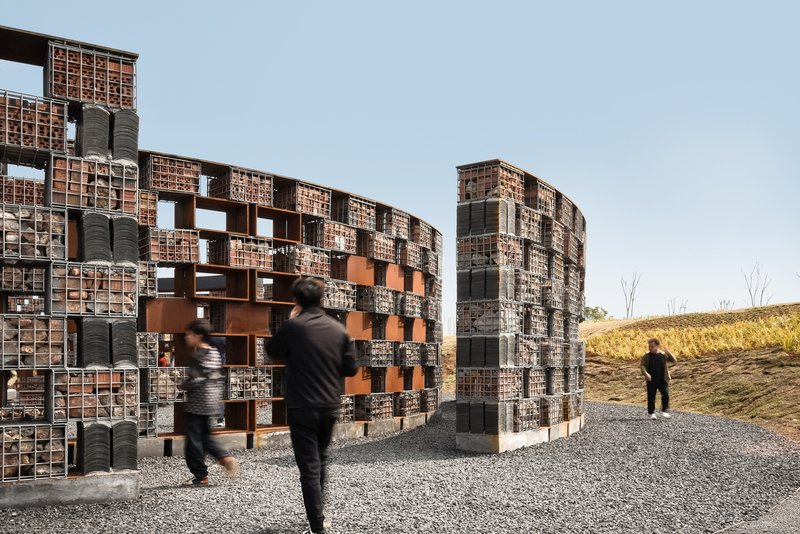 Curved gabion walls with stone fill and terracotta openings on a hillside with dry grass and bare trees