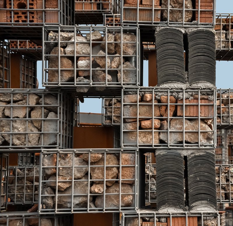 Detail of gabion baskets filled with stone fragments and stacked roof tiles framed by steel mesh
