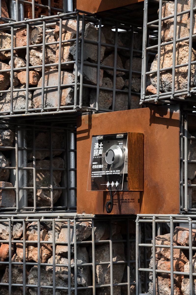 Intercom box mounted on a wall of stacked steel crates filled with stone rubble in daylight