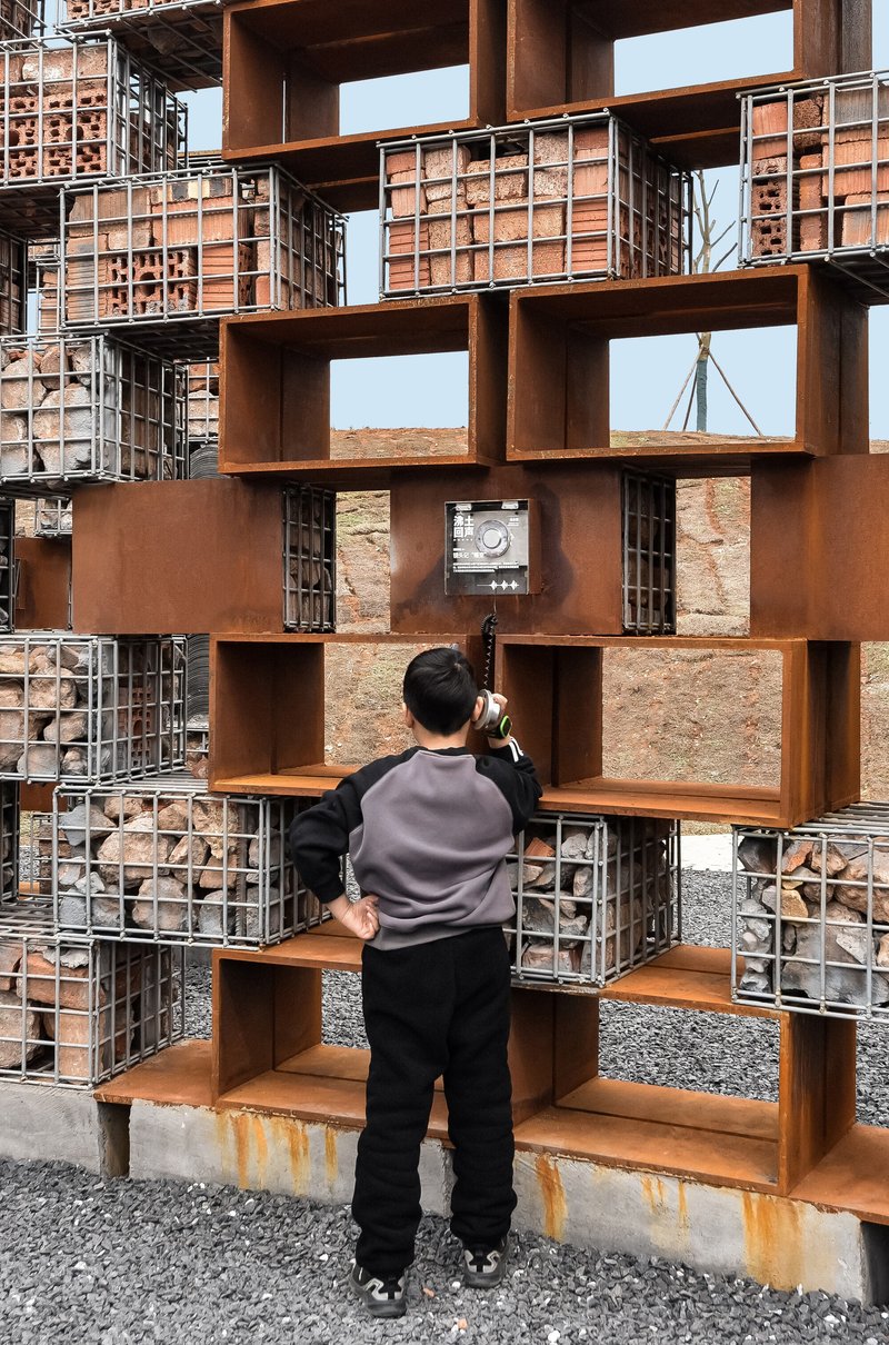 Visitor photographing through layered weathered steel box frames and brick infill panels