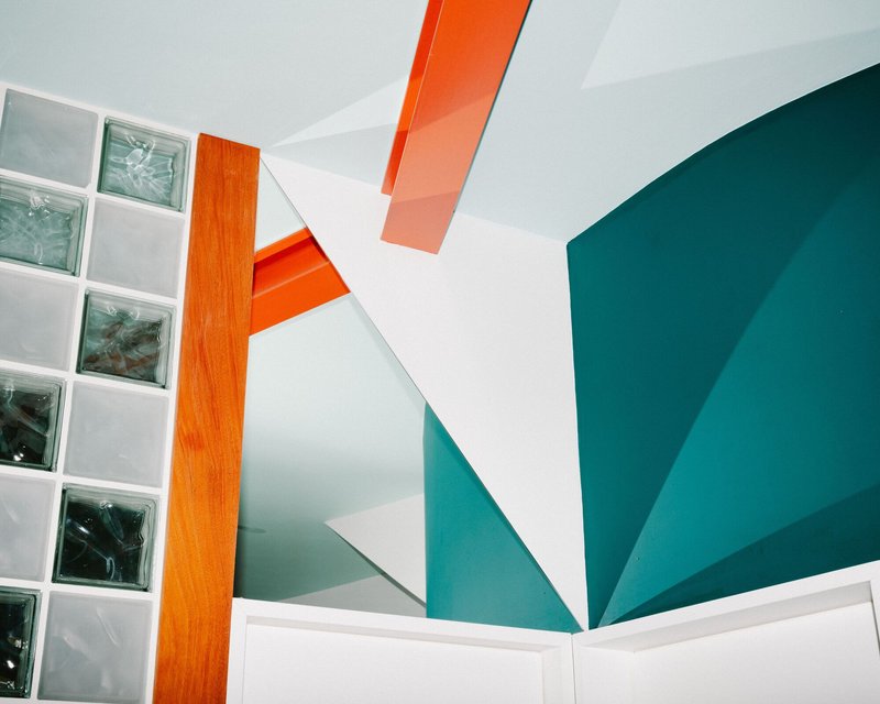 Ceiling detail with radiating teal painted planes, orange beam, and glass block window