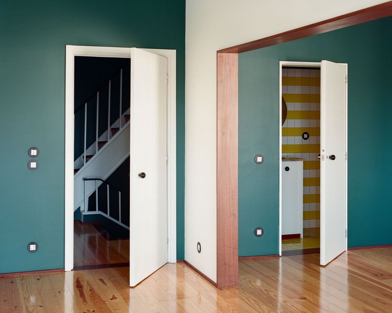Teal-walled room with three white doorways opening to a staircase, storage, and hallway with tile floors