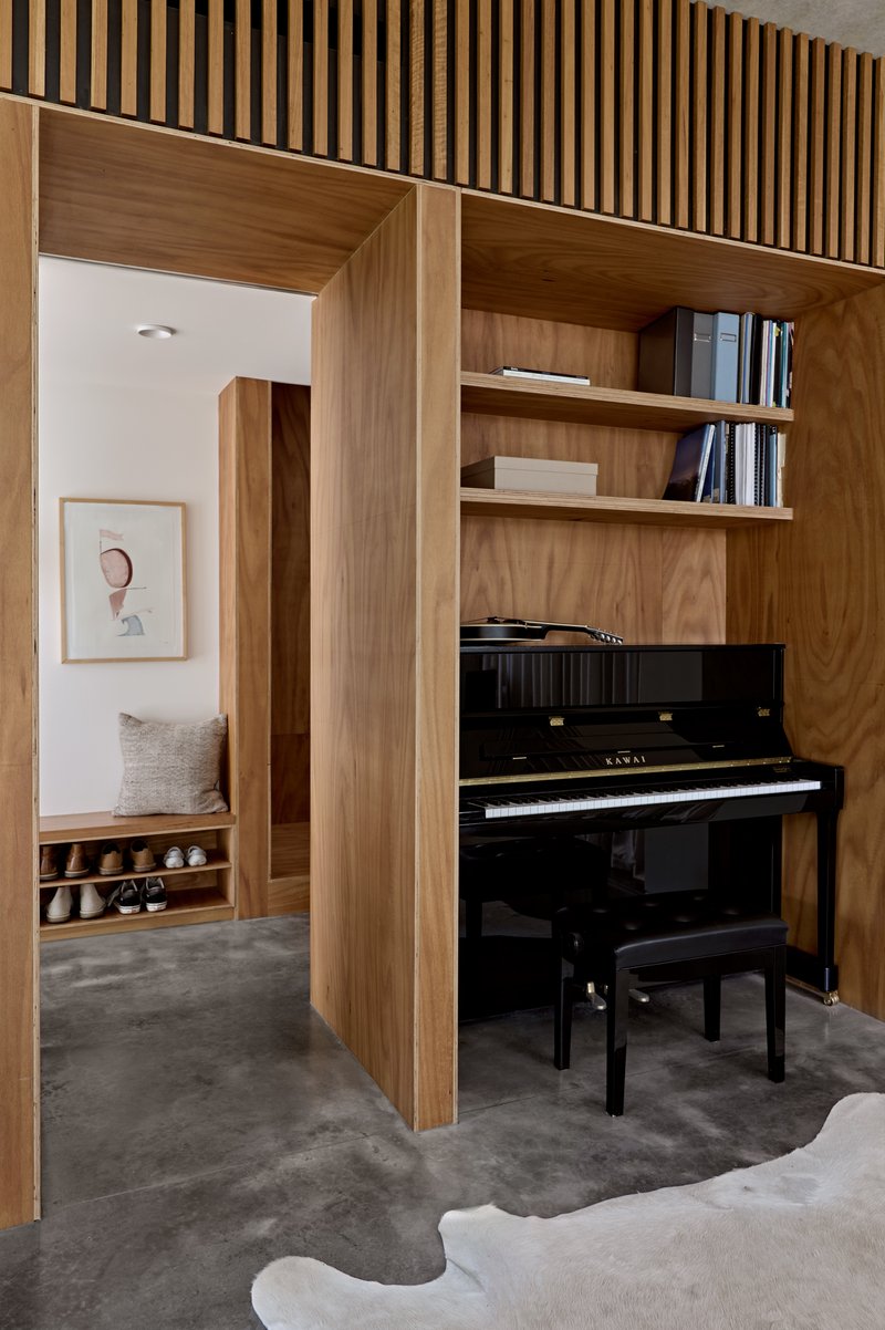 Study nook with upright piano set within timber joinery and view through to bedroom hallway