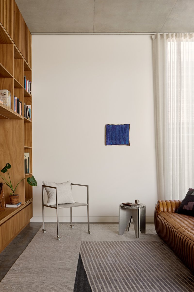 Living room with timber bookshelf wall, concrete ceiling, and sheer curtains beside a striped rug