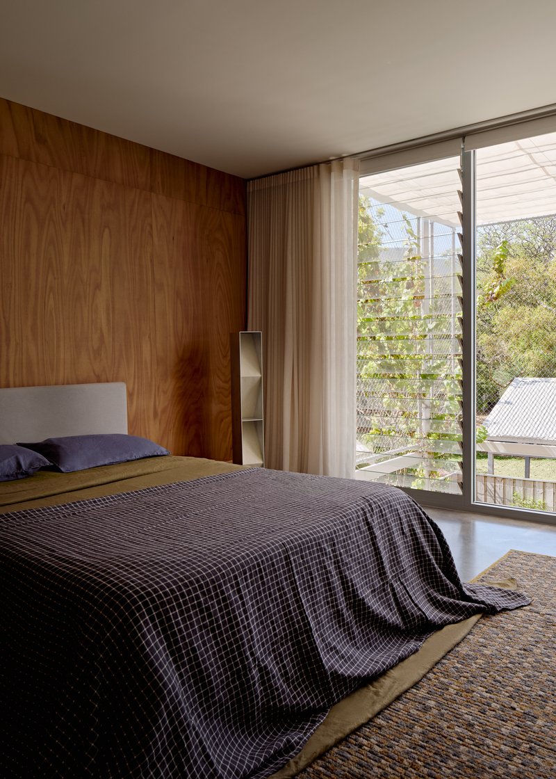 Bedroom with timber wall paneling and louvered windows overlooking neighboring rooftops