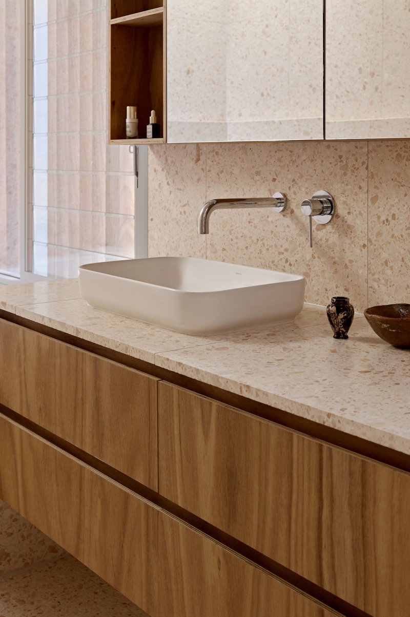 Bathroom vanity with pale stone countertop, timber cabinetry, and wall-mounted chrome tapware