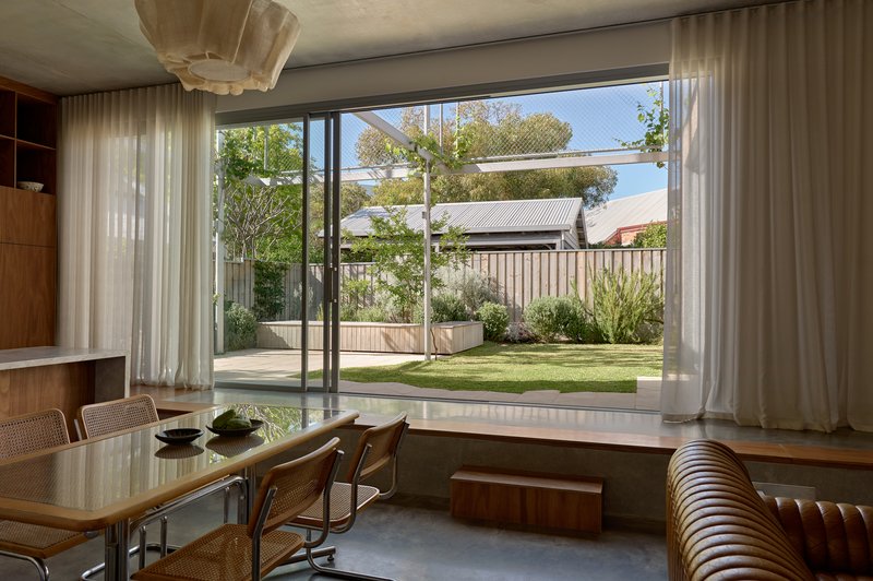 Dining area with floor-to-ceiling glazing framing a view of the planted rear garden and timber fence