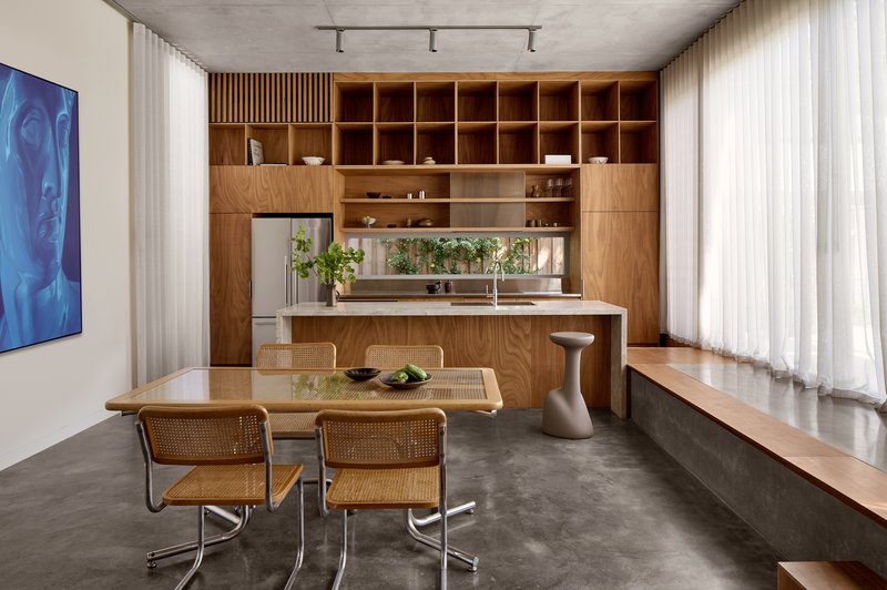 Open-plan kitchen and dining area with timber cabinetry, concrete floor, and floor-to-ceiling sheer curtains